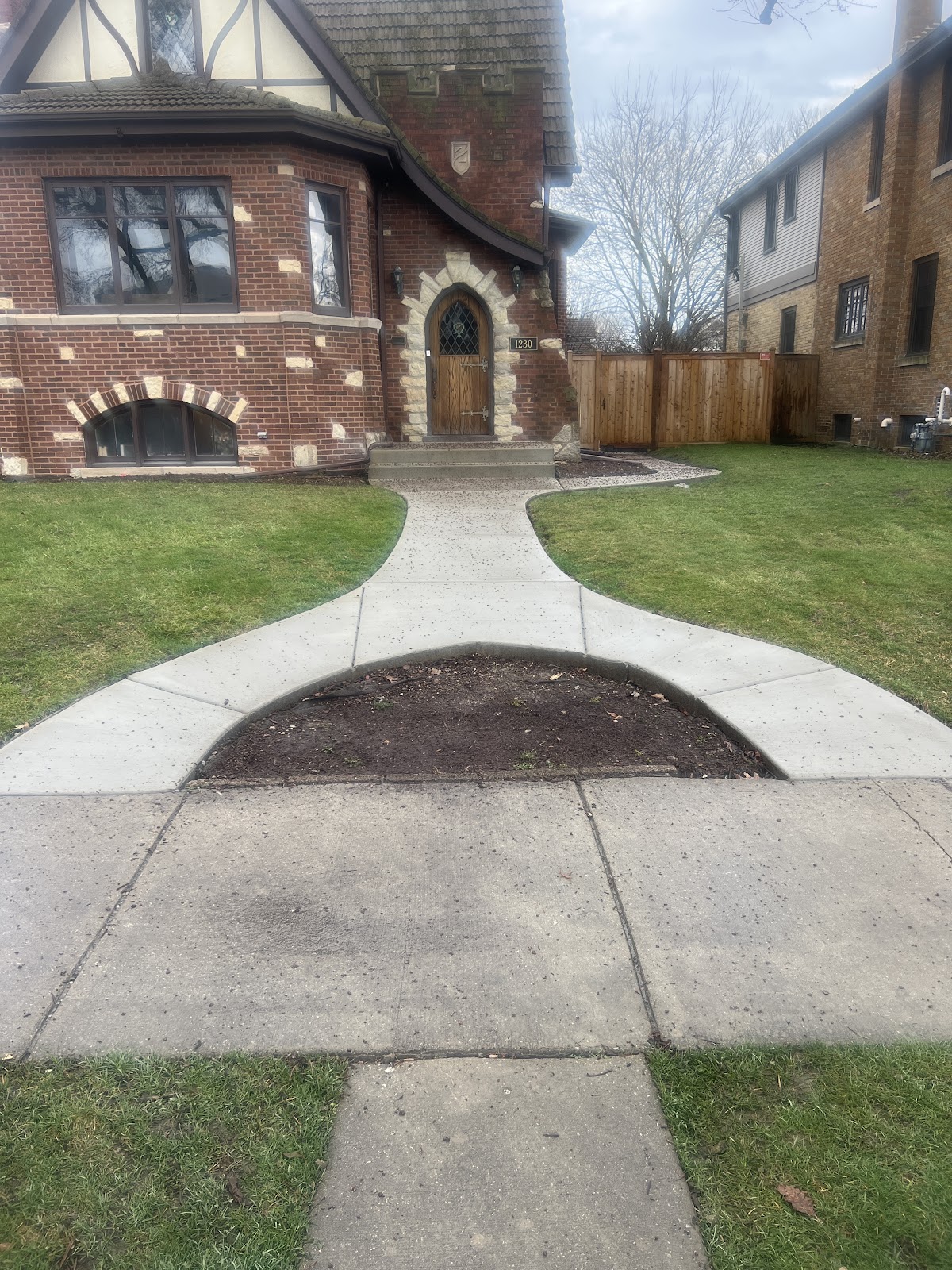 Finished curved concrete walkway leading to a brick home