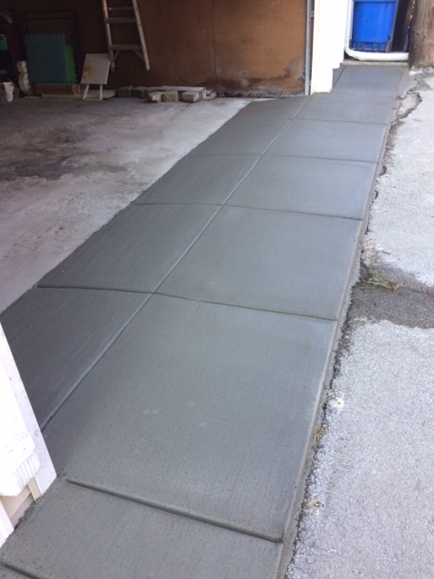Freshly poured concrete walkway beside a garage